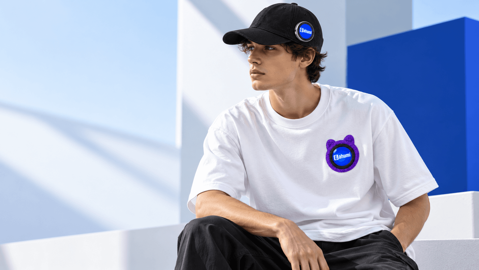Illustrative fashion campaign showing a white display T-shirt with a purple left-chest patch and a black cap with a side-mounted silver-framed screen